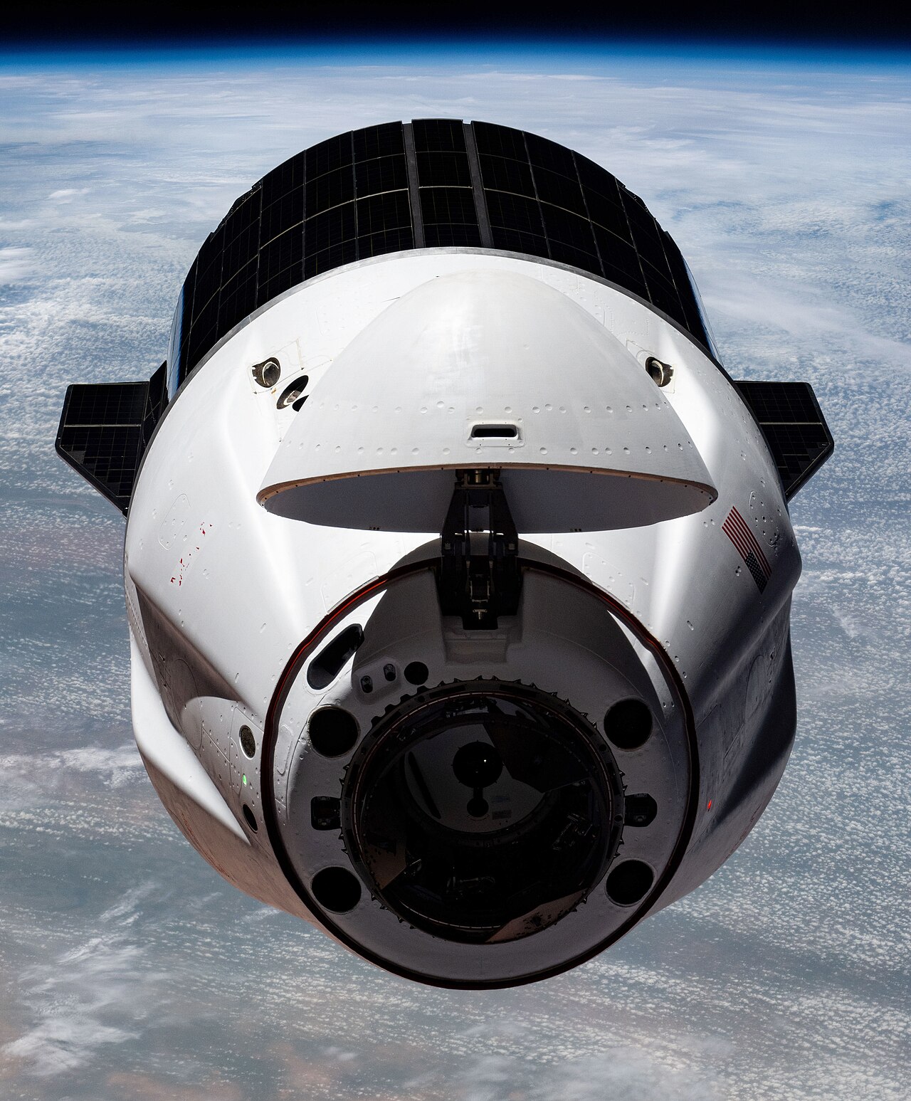 A SpaceX Dragon cargo ship with its nose open, above the Earth.